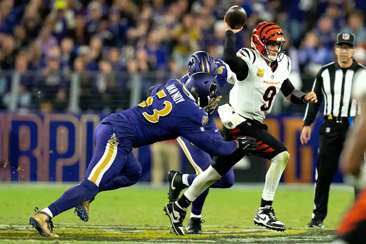 A Cincinnati Bengals quarterback prepares to throw the football as two Baltimore Ravens defenders attempt to tackle him during a game.