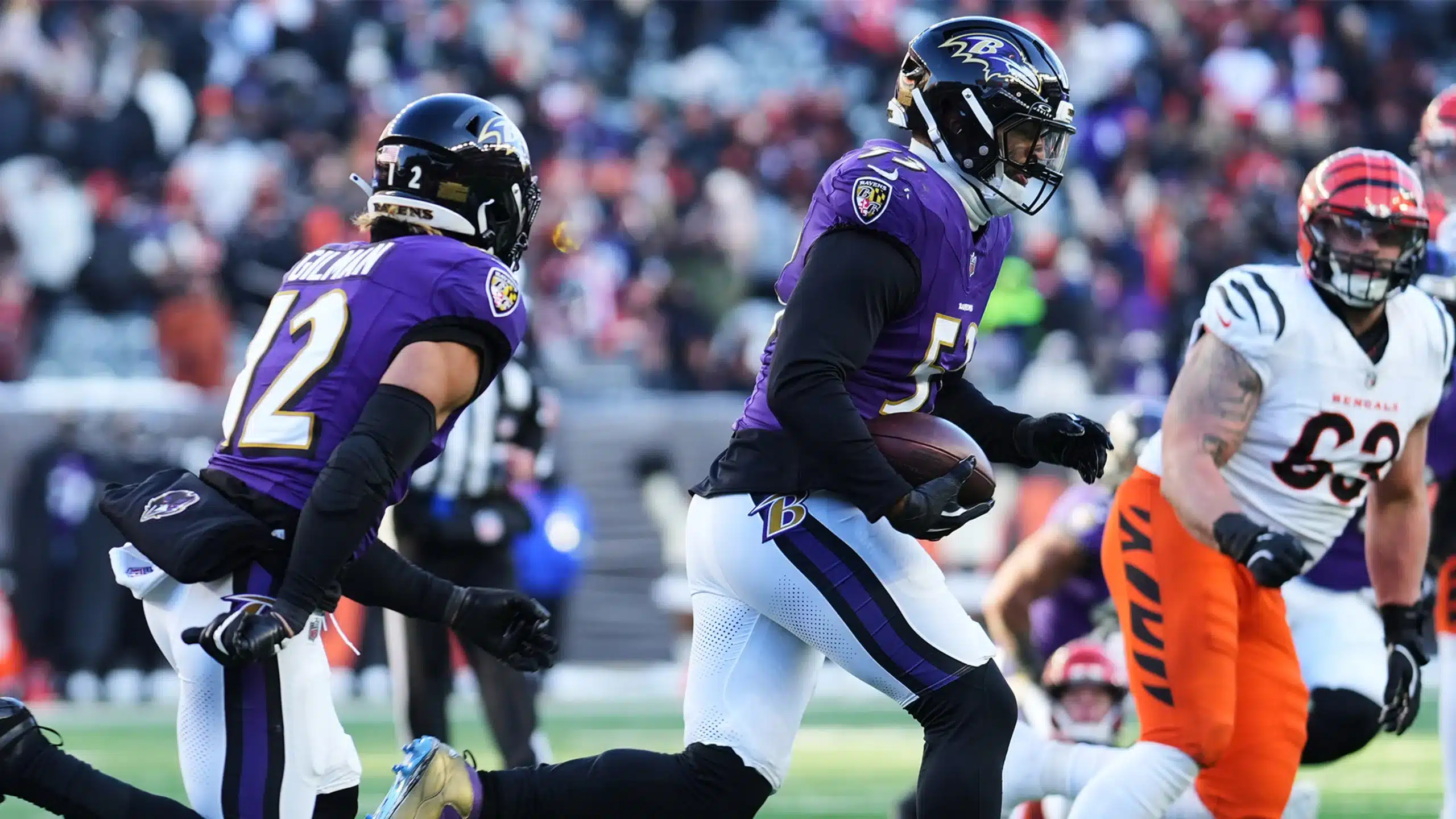 Two Baltimore Ravens football players, Gilman and Van Noy, in purple uniforms run with the ball during a game against the Cincinnati Bengals, whose players wear orange and white uniforms.